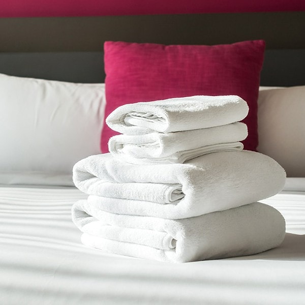Folded white towels on fresh white bed linen in a hotel room